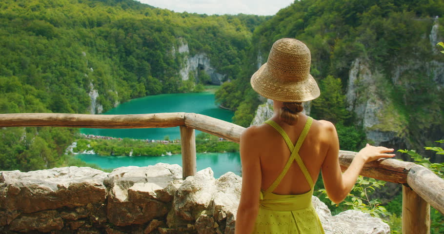 Young elegant woman in dress admires the turquoise waters and cliffs of Plitvice Lakes National Park Croatia