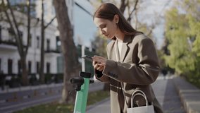 A young professional woman in a stylish coat uses her smartphone while standing by a docked electric scooter on a tree-lined city street, embodying modern urban mobility and connectivity. - Powered by Shutterstock - Get 15% off with code: PIKWIZARD15