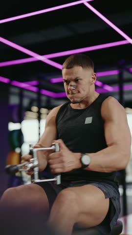 A muscular man performs seated cable rows in a modern gym with vibrant purple lighting. He is focused and determined, pulling the handles with effort, showcasing strength and dedication to fitness.