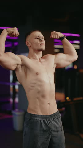 Muscular man shows off his physique and flexes his muscles in a modern gym with neon lighting. He exhales and jumps rope. Ideal for workout, gym, bodybuilding and sports projects.