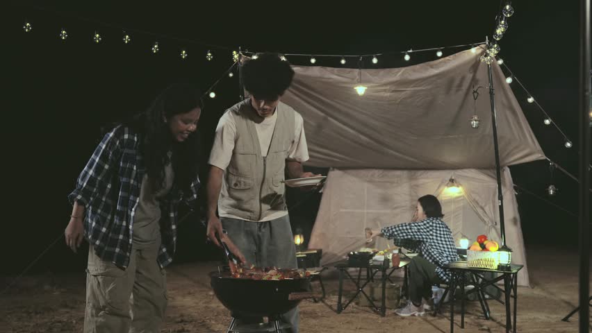 A man and a woman are cooking food on a grill. The woman is wearing a plaid shirt
