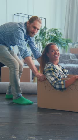Young diverse couple joyfully embraces their move into a new home, playfully using cardboard boxes as part of their fun-filled unpacking adventure together.