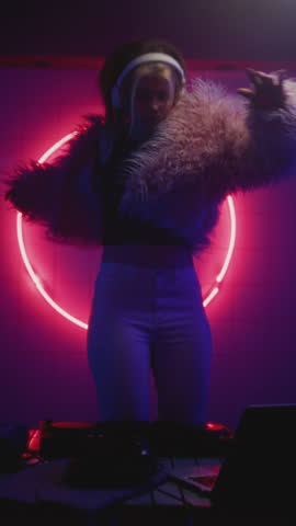 Woman DJ dancing in night neon party. Female disk jockey playing electronic music on techno rave, wear fur coat. Young girl jumping on set or stage, club mixer controller. Artist make modern sound