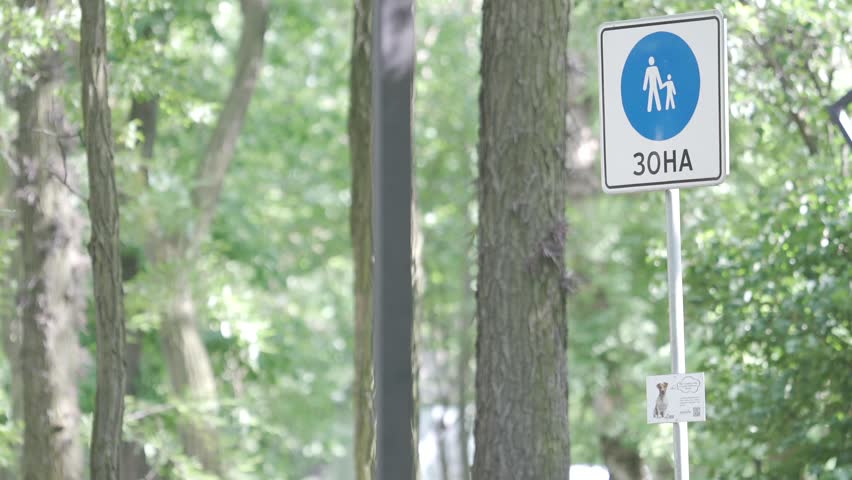 A sign indicating a pedestrian area features a walking figures icon. Situated amidst vibrant greenery, the scene captures a serene atmosphere under clear skies.