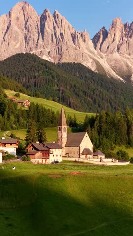 vertical video of Italian Dolomites iconic chapel of St Maddalena, drone shot of church in Santa Magdalena at sunset in the Dolomites, Italy, idyllic alpine meadow. 