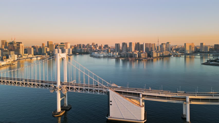 tokyo city skyline aerial shot drone at sunrise view of the waterfront with high office buildings seen from the sea with rainbow bridge in the foreground