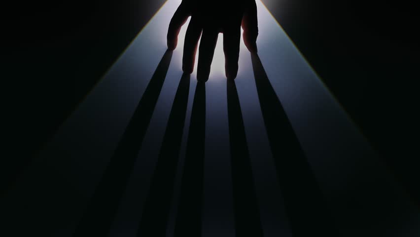 A silhouetted hand casts dramatic shadows in dim lighting, evoking mystery and creativity. Slow motion