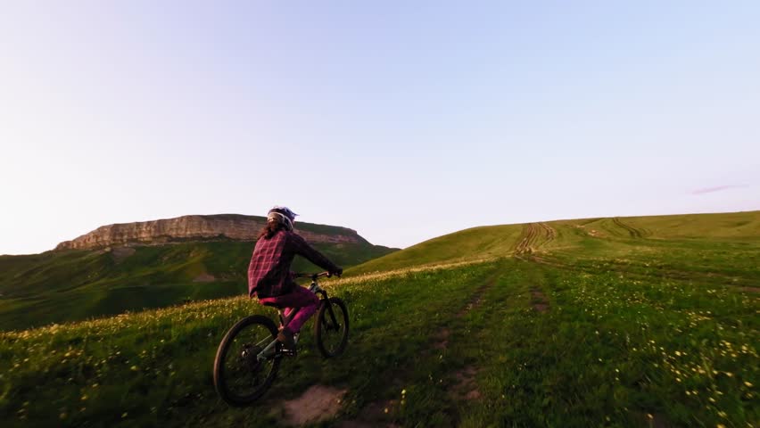 Young male rider doing wheelie on his bicycle in slow motion in mountains. Aerial view from fpv drone with epic rocky mountains
