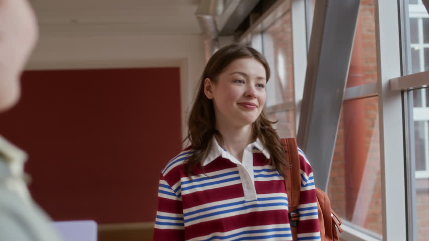 Handheld shot of three multiethnic gen Z girlfriends greeting each other before classes in hall of university