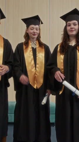 Vertical shot of intercultural zoomers in academic wear throwing hats up in university hall after commencement