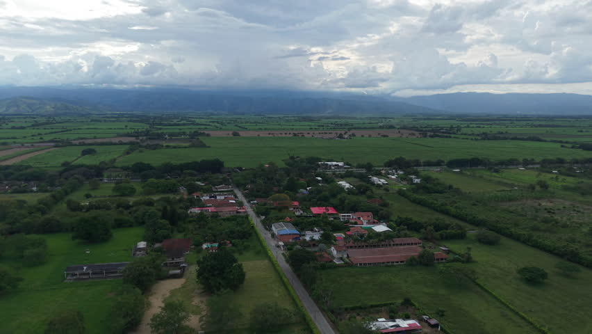 Stunning aerial footage showcases the lush green landscapes and quaint town of Los Chancos, Valle del Cauca. Clouds cast soft shadows under natural lighting, adding to the serene ambiance.