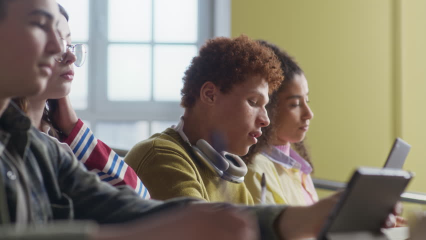 Handheld shot of group of diverse collegemates using digital devices during lecture in auditorium