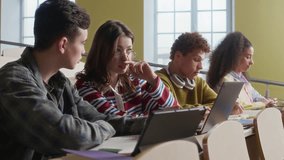 Medium shot of four gen Z multiethnic peers sitting at tiered desk studying with digital gadgets in lecture hall - Powered by Shutterstock - Get 15% off with code: PIKWIZARD15
