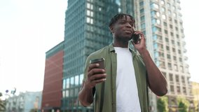 Smiling African American young man talking on mobile phone while holding coffee outdoors. Male in casual outfit standing in city center and chatting on telephone. Enjoying conversation and urban vibes - Powered by Shutterstock - Get 15% off with code: PIKWIZARD15