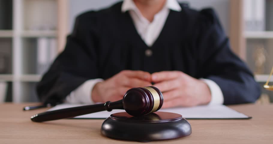 Man judge wearing judicial robe knocking gavel having court verdict sitting at the desk on workplace in courtroom. Male justice worker working indoors. Legal law and justice concept. 4k video.