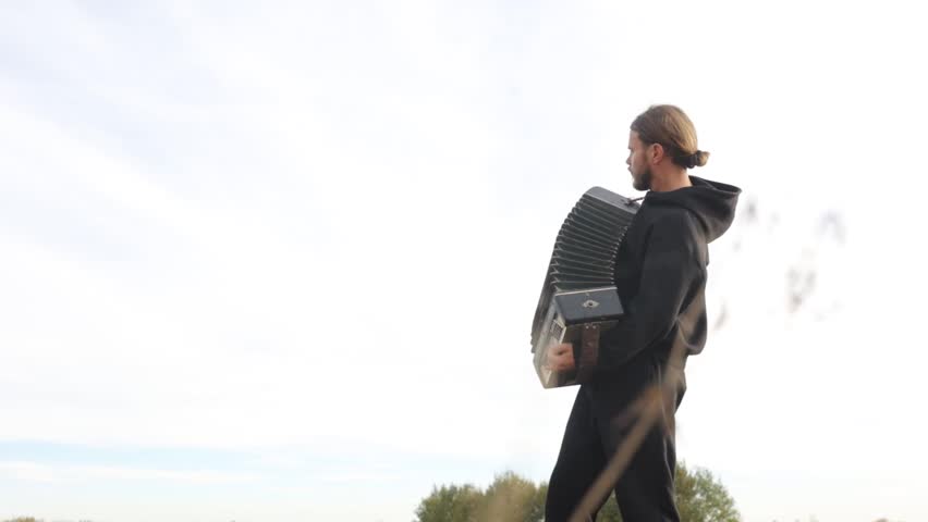 man plays the accordion in a field in nature