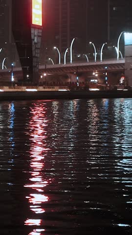 Walking along the beautiful embankment at night in the Persian Gulf in the Middle East. Reflections in the water from the neon evening city with skyscrapers. Yachts and ships in the Dubai, UAE