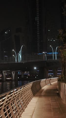 Walking along the beautiful embankment at night in the Persian Gulf in the Middle East. Reflections in the water from the neon evening city with skyscrapers. Yachts and ships in the Dubai, UAE