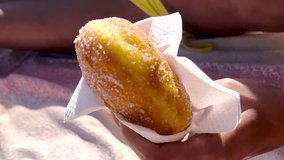 Hand holding a malasada donut with sugar at a beach food stand, close-up of fast food in colorful wrapper, yellow bikini - Powered by Shutterstock - Get 15% off with code: PIKWIZARD15