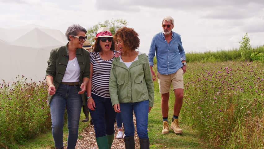 Group Of Smiling Mature Friends Walking Along Path Through Yurt Campsite