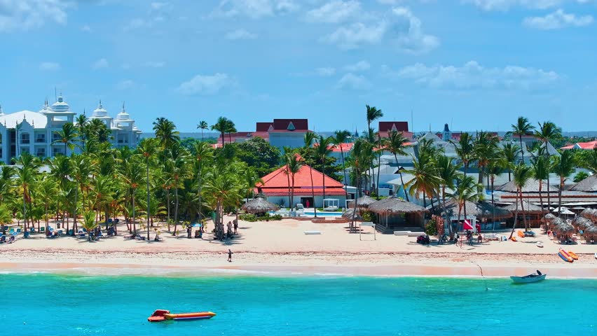 Dominican Republic resort beach background with colorful palm trees on white sand. Orange boat on turquoise sea on a summer sunny day near paradise coast. Relaxing by the sea.