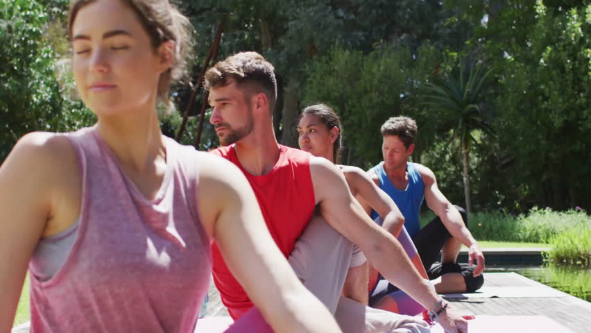 Fitness group holding seated twist by pond deck, generating floating heart emojis for engagement. Outdoor, wellness, serenity, harmony, meditation, nature, relaxation