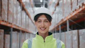 Smiling Caucasian woman wearing white helmet and safety jacket posing in warehouse aisle. Standing confidently between shelves packed with sealed boxes. Professional team leader or supervisor. - Powered by Shutterstock - Get 15% off with code: PIKWIZARD15