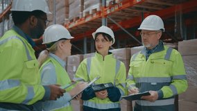 Four warehouse workers wearing safety gear discussing logistics while holding scanner, tablet, and clipboards. Team standing between tall shelves filled with stacked cardboard boxes and pallets. - Powered by Shutterstock - Get 15% off with code: PIKWIZARD15