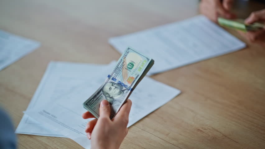 Businesspeople exchanging dollars euro in office buro closeup. Woman banker hands giving pack of cash to male client indoors. Entrepreneur receiving money from colleague at wooden table workplace