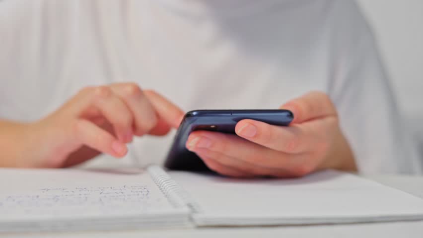 Person using smartphone while taking notes in a notebook at a desk