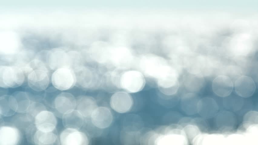 Blurred light blue background round bokeh with sparkling sunlight and shimmering sun glare on blue surface of water. Natural defocused background with sun shine. Abstract Sea Day. Meditation relax