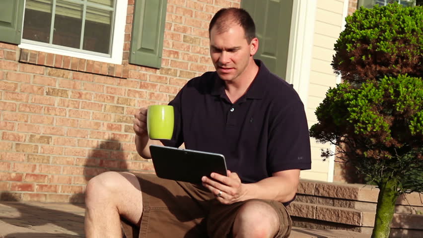 A man uses his tablet PC outside the house, perhaps reading the paper.
