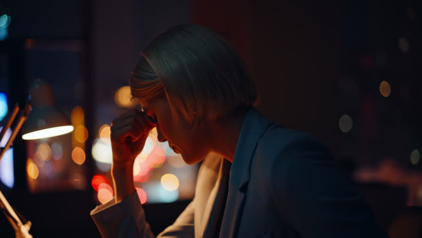 Exhausted late businesswoman feeling burnout sitting in dark workspace closeup. Fatigued office worker touching head unmotivated to overtime work. Tired blonde having headache migraine at hard workday