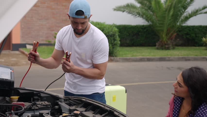 Young couple facing car trouble, trying to jumpstart their vehicle with jumper cables during a road trip