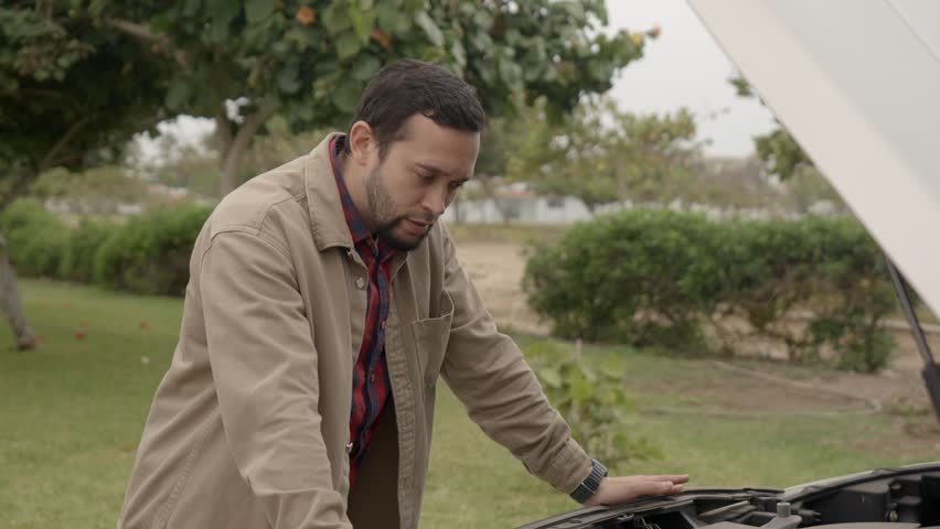 Worried tourist inspecting his car engine after a breakdown during a road trip, trying to identify the mechanical issue