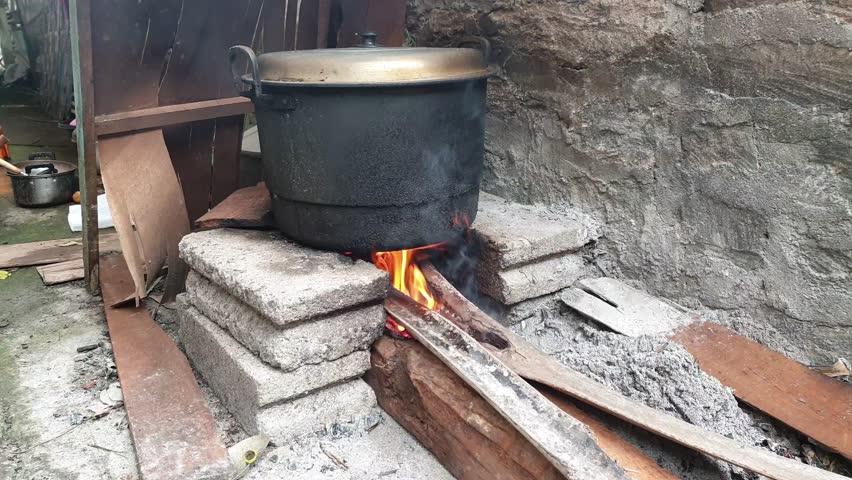 Traditional outdoor cooking uses a black pot heated on a stone stove and a fire source of firewood.