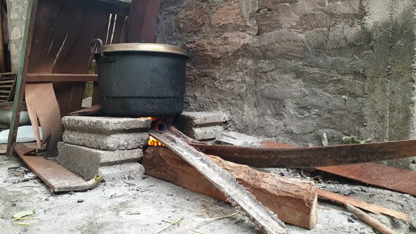 Traditional outdoor cooking uses a black pot heated on a stone stove and a fire source of firewood.