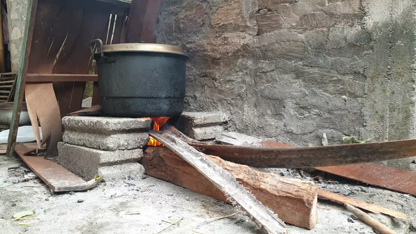 Traditional outdoor cooking uses a black pot heated on a stone stove and a fire source of firewood.