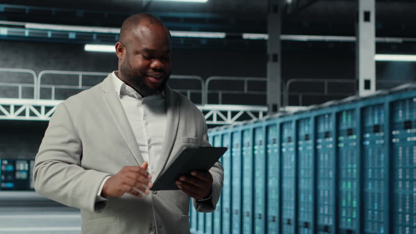 Smiling data center technician installing upgraded server racks systems using tablet. Upbeat server room worker monitoring infrastructure performance using automation tools on device, camera B