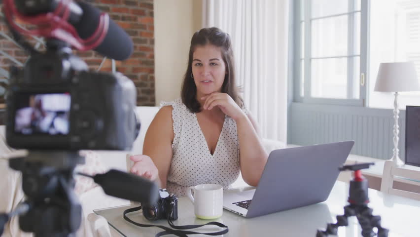Content creator speaking to camera in office, summoning floating reaction icons, typing on laptop. Studio, communication, technology, influencer, productivity, digital, modern