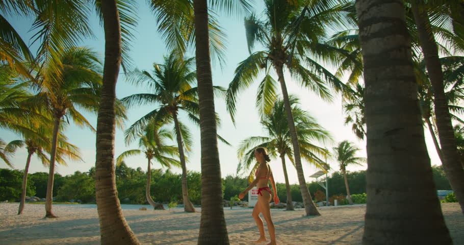 Woman walking on a sandy tropical beach surrounded by palm trees in Yucatan Mexico