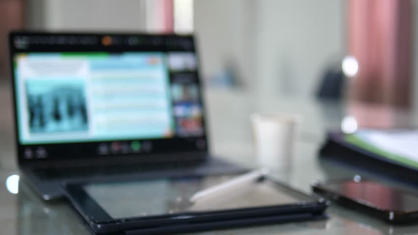 Blurred video call on laptop screen with coffee and tablet on desk in modern office