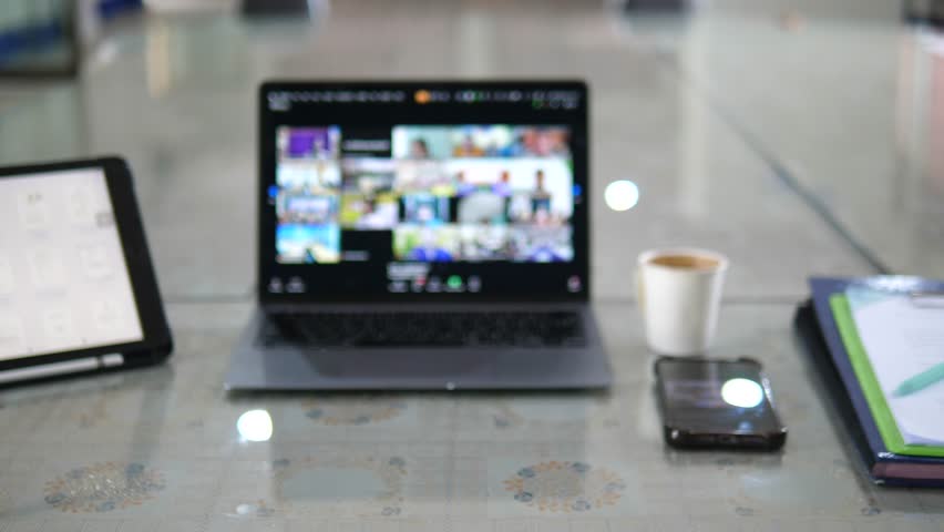 Blurred video call on laptop screen with coffee and tablet on desk in modern office