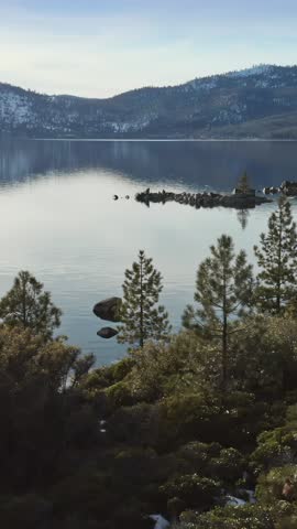 Scenic view of Lake Tahoe, California, USA. Calm waters reflect the snow-capped mountains and evergreen trees, capturing the serene beauty of the natural landscape.