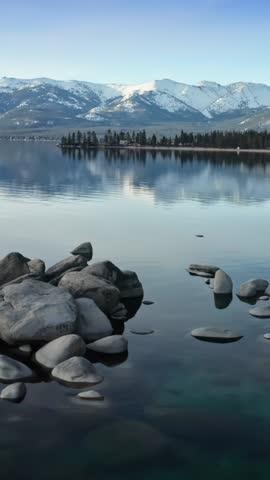 Lake Tahoe, USA: People relax on the rocks along the shoreline, enjoying the calm water and mountain views. Tourists visit to experience the natural beauty.