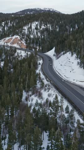 Cars travel along a highway through a snowy, mountainous, forested landscape in the United States. The road provides access through the remote terrain.