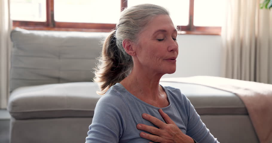 Senior woman meditating at home, finding peace and relaxation in living room. Meditation, mindfulness, tranquility, elderly, wellness, serenity