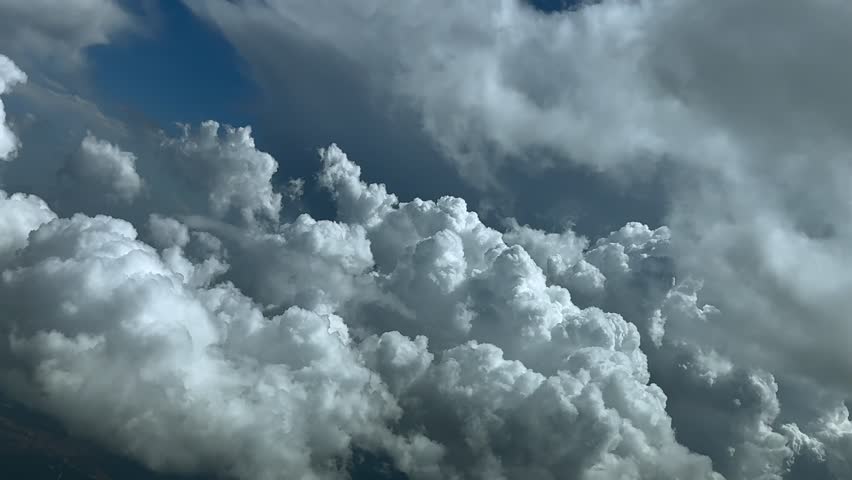 An immersive cockpit view of a real time flight through the pilot eyes while flying through a stormy sky with cottony clouds under an intense blue color sky at sunset. Ultra-realistic 4K scene.