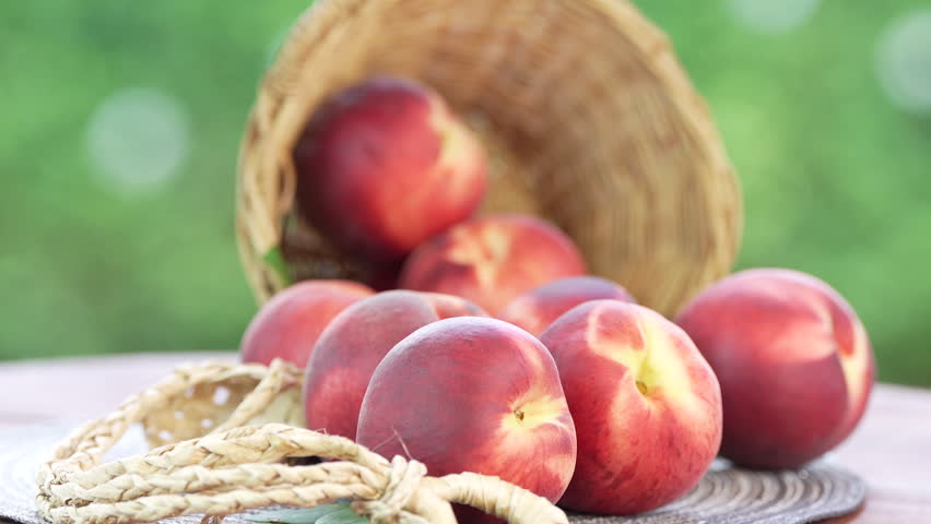 Fresh peach with slices on blurred greenery background, Peach fruit in Bamboo basket on wooden table in garden.