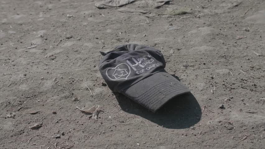 A dirty cap from the 'Hope and Homes for Children' charity lies discarded on the ground, a poignant and ironic symbol of lost hope, childhood poverty, and social crisis.
